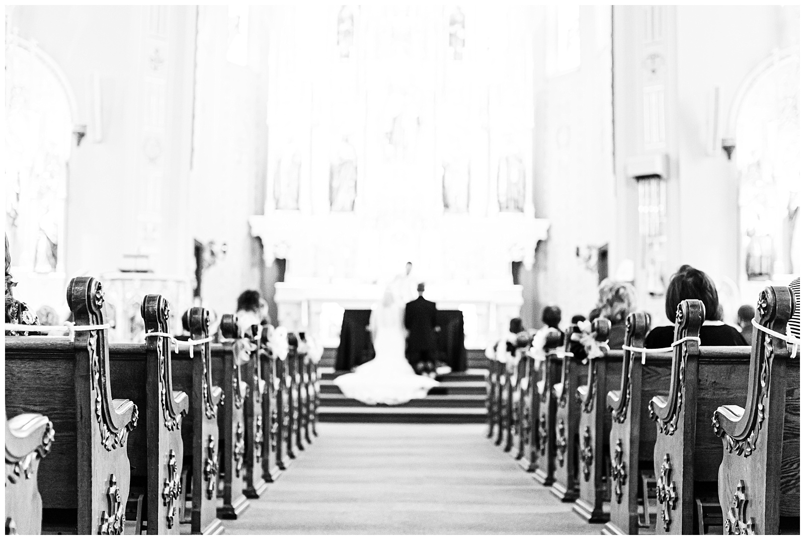 black and white focusing on the sides of the pews with the bride and groom kneeling at the end of the aisle