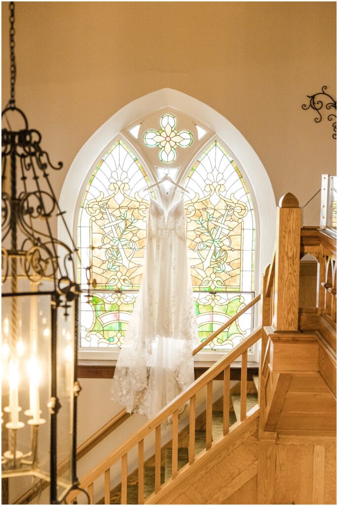 a wedding dress hanging in the stained glass window of an old church